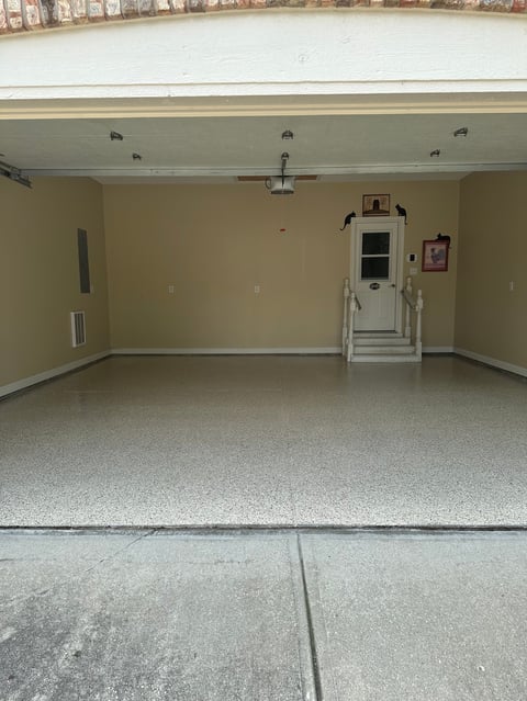 Empty two-car garage interior with yellow walls, concrete floor, and white door with decorative items on back wall