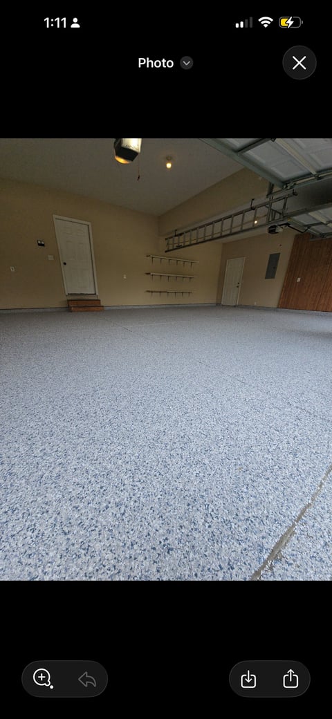 Empty garage interior with epoxy flooring, wall-mounted tool racks, white doors, and overhead storage ladder system