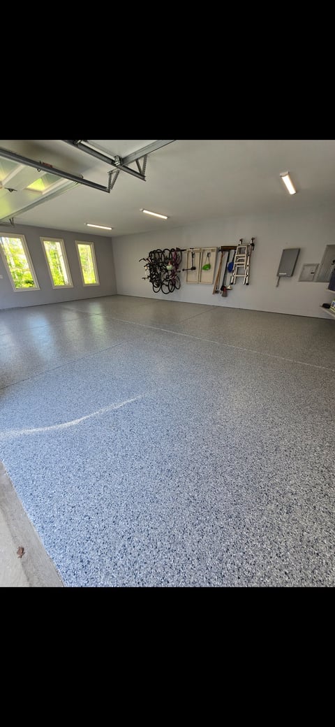 Modern garage interior with polished gray epoxy floor, wall-mounted bikes and tools, LED ceiling lights, and three windows