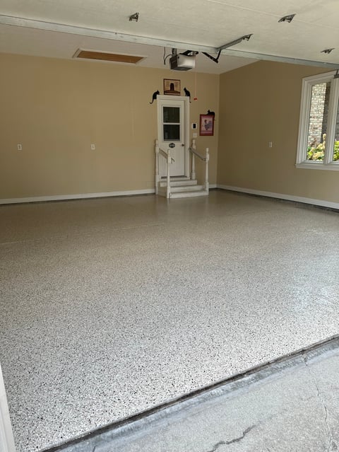Empty residential garage with concrete floor, beige walls, and white door with small shelving unit in center